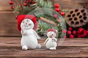 Two snowman figurines in red hats, white snowflakes on a dark wooden textured background. Christmas toys