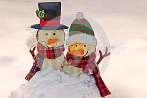 two snowmen decorations with carrot noses, hats and scarves in Winter snow
