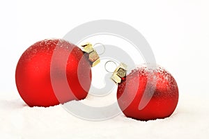 Two snowy red christmas matt balls standing on snow on white background