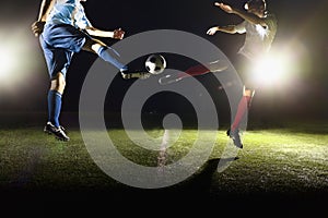 Two soccer players kicking a soccer ball at game