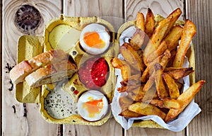 Two soft boiled eggs with fries and sauces.