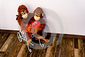 Two soft toy monkeys sit arm in arm in a small car, holding a fabric heart in their hands Landscape
