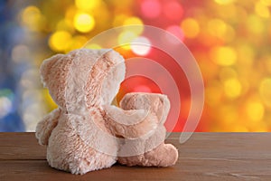 Two soft toys bears are sitting on brown wooden background. Blurred bokeh background