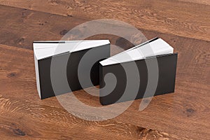 Two softcover or paperback horizontal or landscape black mockup books standing on the wooden background. Blank front and back