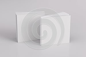 Two softcover or paperback square white mockup books standing on the white background. Blank front and back cover