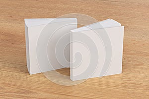 Two softcover or paperback square white mockup books standing on the wooden background. Blank front and back cover
