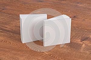 Two softcover or paperback square white mockup books standing on the wooden background. Blank front and back cover