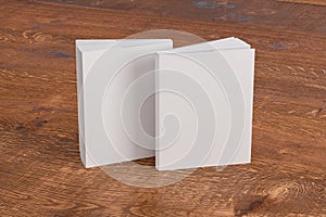 Two softcover or paperback vertical white mockup books standing on the wooden background. Blank front and back cover