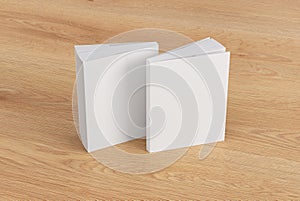 Two softcover or paperback vertical white mockup books standing on the wooden background. Blank front and back cover