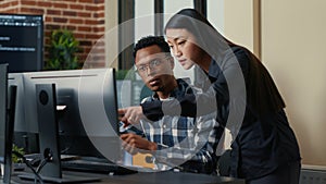 Two software developers coming at desk and sitting down holding laptop with coding interface