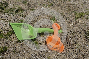 Two spades, shovel, green and orange - children`s beach toys on stony beach with seaweeds. Close up view
