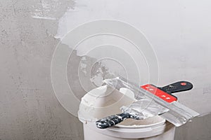 Two spatulas for wall repairs lie on a bucket against the background of the wall, a place for an inscription