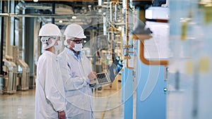 Two specialists in lab coats are operating factory equipment