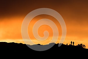 Two spectators standing on a hilltop watching sunset