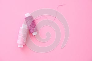 Two spools of sewing thread lilac pink, violet, crimson on a pink paper backgroun