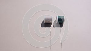 Two spools of sewing thread in pleasant beige and green on a harmonious sandy background.