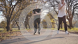 Two sportive Caucasian boys running in the autumn park. Adult sportsmen stopping because of pain in heart. Healthy