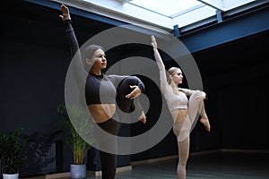 Two sportive women lifting legs, raising their legs and doing stretching exercises at gym