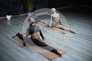 Two sportive women practicing doing split together in stretching studio