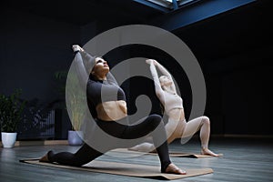 Two sportive women standing on floor mat on knees, throwing head back