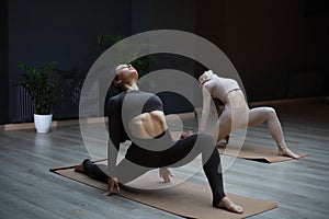 Two sportive women standing on floor mat on knees, throwing head back