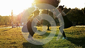 Two sports women training and squat together in the park at sunset. Fitness, aerobics and stretching exercises, healthy