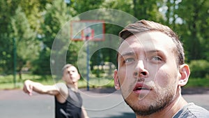 Two sportsmen playing basketball on the court outdoors - one man throwing the ball - other man watching him