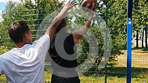 Two sportsmen playing basketball on the court outdoors, one sportsman dribbling and missing past the basket