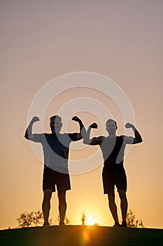 The two sportsmen showing muscles on the sunset background.