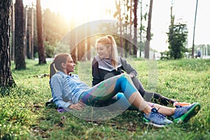 Two sporty girlfriends relaxing, lying on grass and chatting in the forest after jogging together