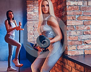 Two sporty girls dressed in sportswear with barbells posing in a