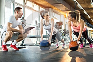 Two sporty girls exercising with fitness balls while their fitness instructor tracking the progress on clipboard.