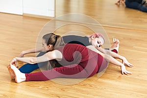 Two sporty girls in gym doing acroyoga, yoga with partner, Wide-Angle Seated Forward Bend, Upavishtha Konasana.