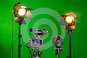 Two spotlights with Fresnel lenses, camcorder and SLR camera on a green background. Shooting in the interior with artificial light