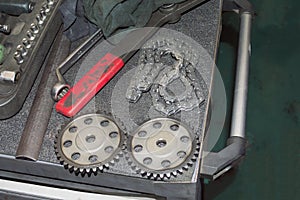 Two sprockets and a chain of the timing chain mechanism lie on a gray tool cart