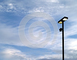 two square light boxes street lamp on metal post against cloudy blue sky