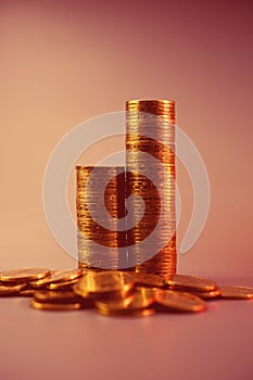 Two stacks of golden coins arranged in ascending order and lying coins on a light pink background