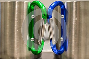 Two stainless mugs with a green and blue carabiner handle touching