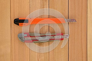 Two stationery knives in orange and red on a wooden background.