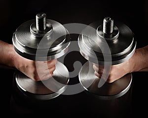 Two steel typesetting dumbbells in male hands, sports backdrop photo