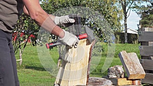 Two Steel Wedges in pine tree Log. Mature caucasian man splitting log with help heavy hammer and wedges when it is not possible to