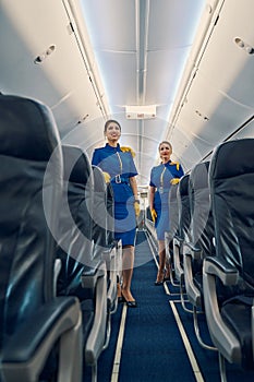 Two stewardesses in uniforms leaning on the airline seats