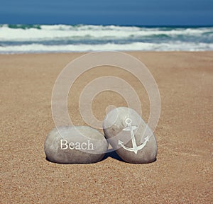 Two stone pebbles with the word beach and anchor sign over sandy beach and sea horizon