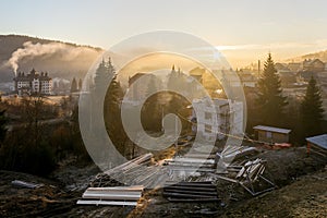 Two-storied house hotel under construction on building site, pile of boards and logs for roofing in ecological rural area on photo