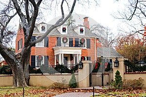 Two story red brick house in upscale leafy residential neghborhood with iron fence and gate beautifully decorated with Christmas w