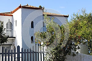 Two story  white Greek stucco house with upstails balcony and picket fence and red tile roof - Close-up