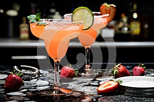 Two strawberry margaritas on a bar, against a dark background.