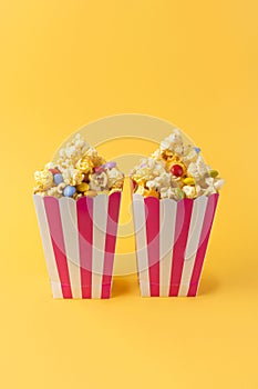 Two striped carton buckets with caramel popcorn and dragee candies on yellow background