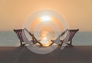 Two striped red-white sunbeds at sandy tropical sunset ocean beach.