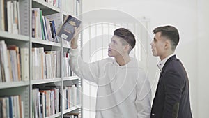 Two studens are Looking For Book On Bookshelves At Library At College